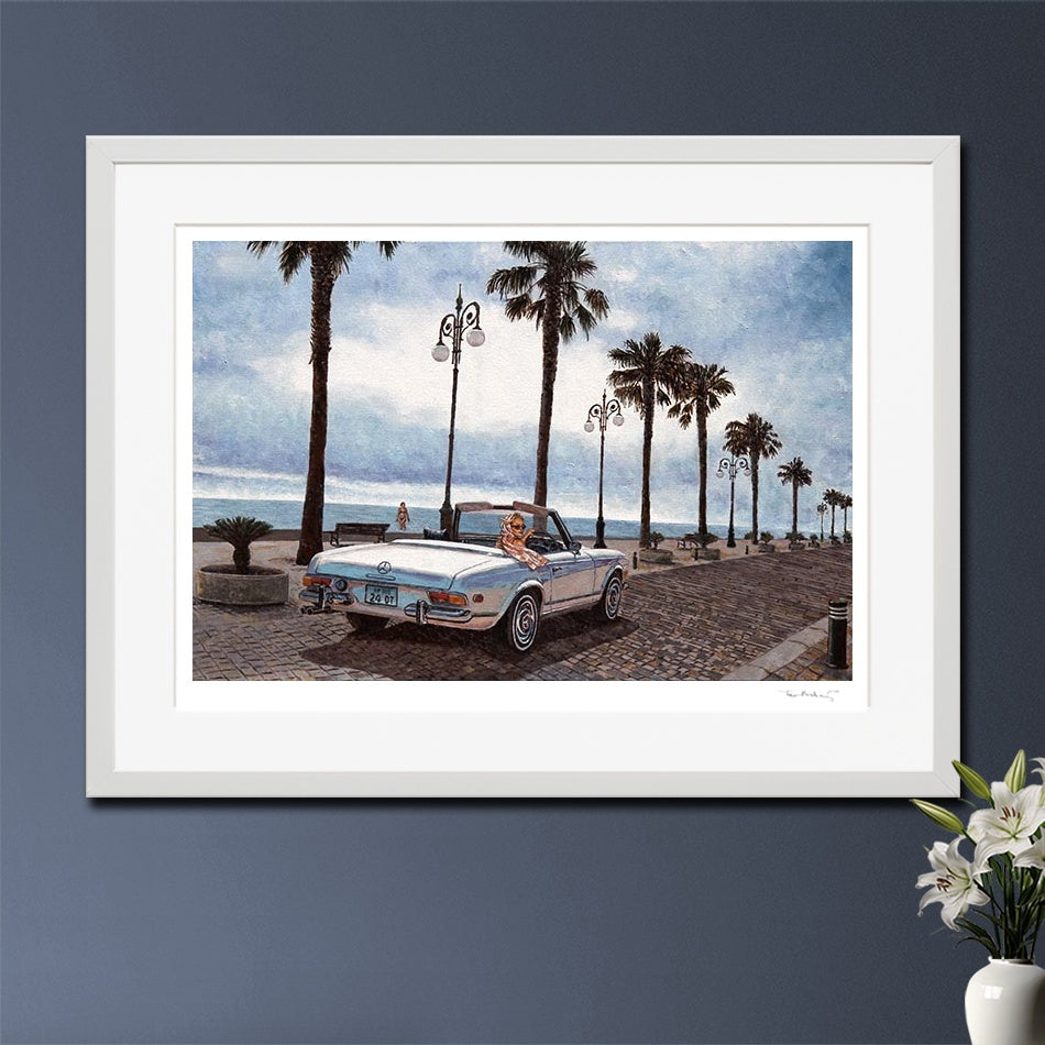 A framed art print depicting a vintage convertible car parked on a palm-tree-lined seaside promenade in Larnaca Cyprus. After an oil painting by Theo Michael